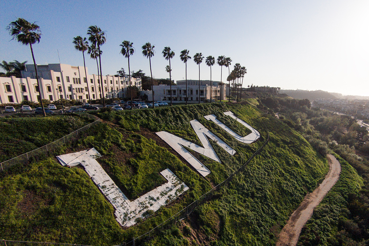 The LMU letters on the bluff with palm trees in the background and a blue sky.